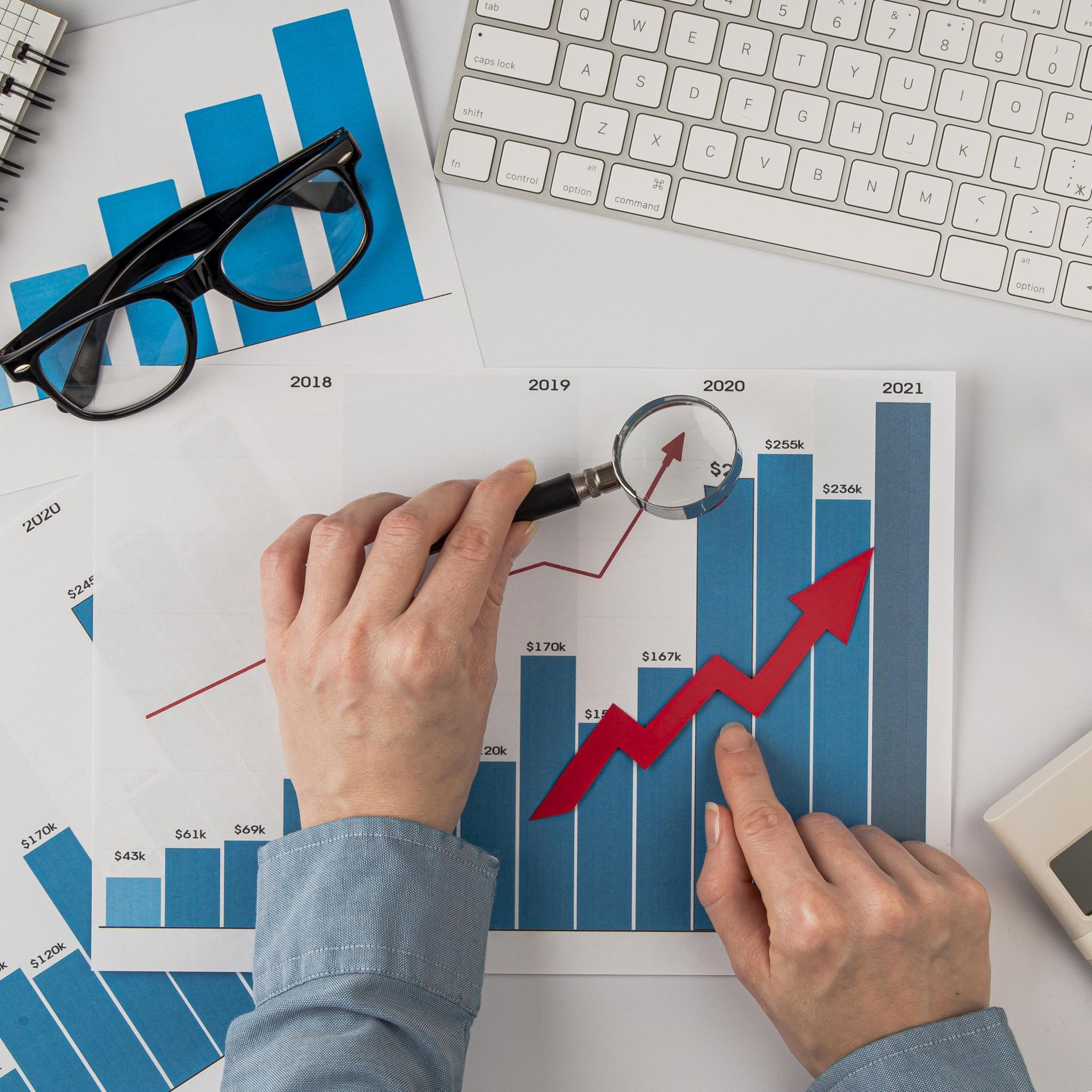 vista-superior-escritorio-oficina-tabla-crecimiento-manos-sosteniendo-lupa